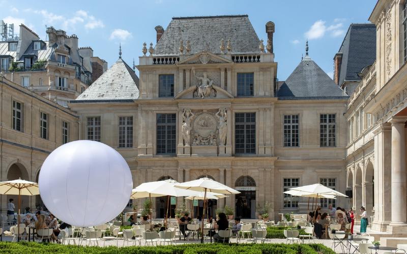 Une table de café parisien avec le livre Notre Dame de Paris 2024, un café et une pâtisserie, sous le soleil matinal